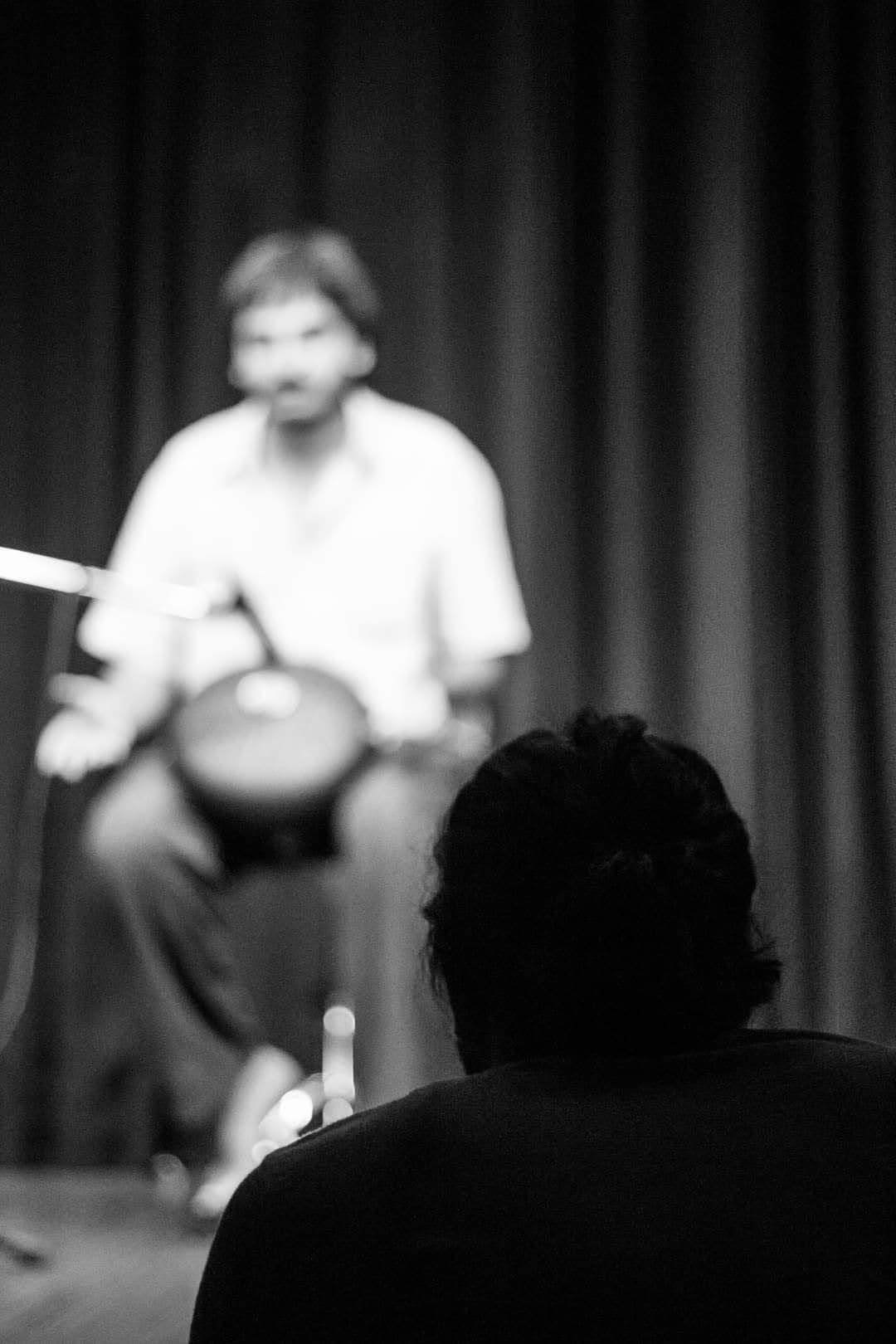 Black-and-white photo from behind an audience member's head, a performer out of focus on stage